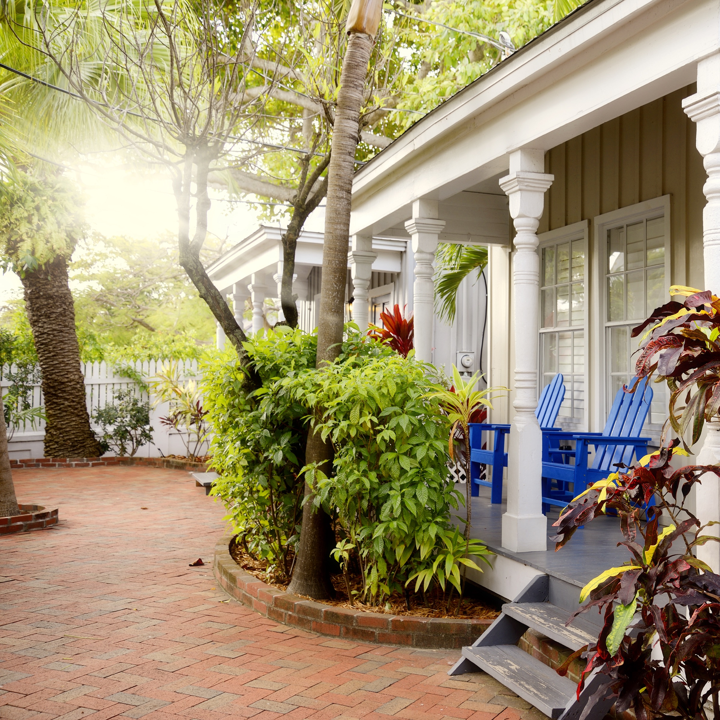 Welcoming Key West porch with blue Adirondack chairs and a brick walkway
